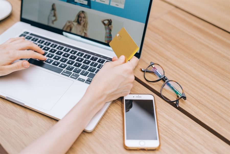 Hands at a laptop holding a payment card next to a phone and glasses